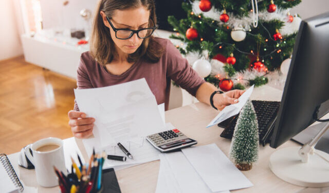 Woman sitting at the office desk and reading letter with christmas tree in the background